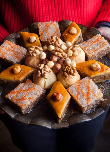 From above assorted baked with baklava and baklava sheki and human hand in copper plate on wood background